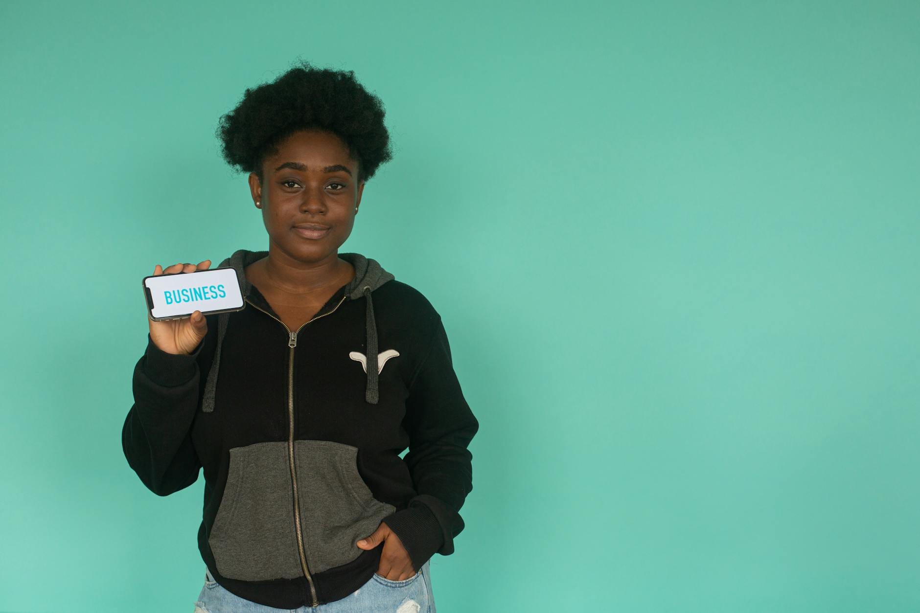Kobieta w bluzie pokazuje smartfon z napisem business na turkusowym tle
