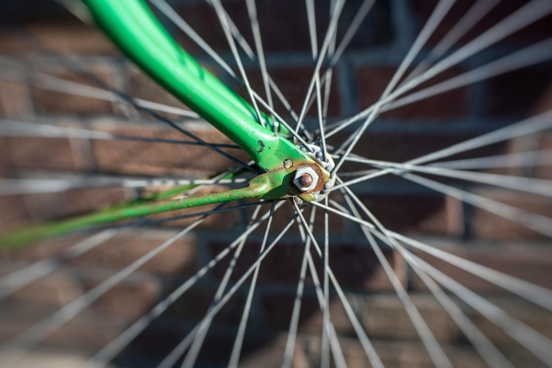Zbliżenie zielonego koła roweru z widocznymi szprychami na tle cegieł
