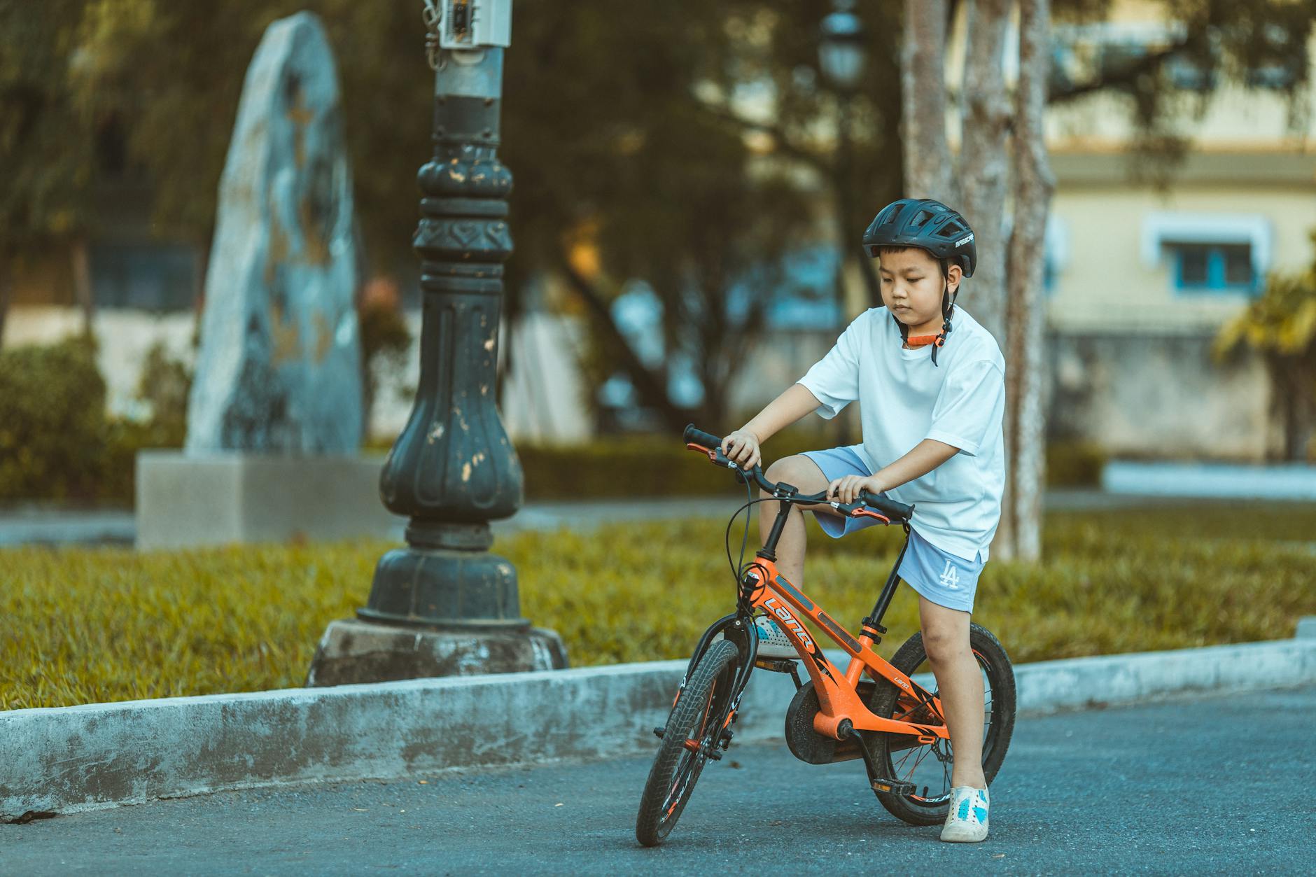Chłopiec w kasku jedzie pomarańczowym rowerem po parku