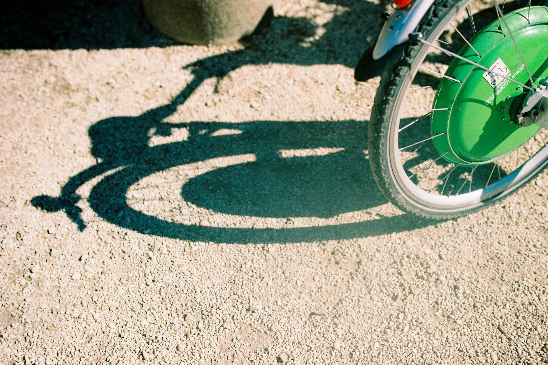 Cień koła rowerowego na żwirowej ścieżce w słoneczny dzień