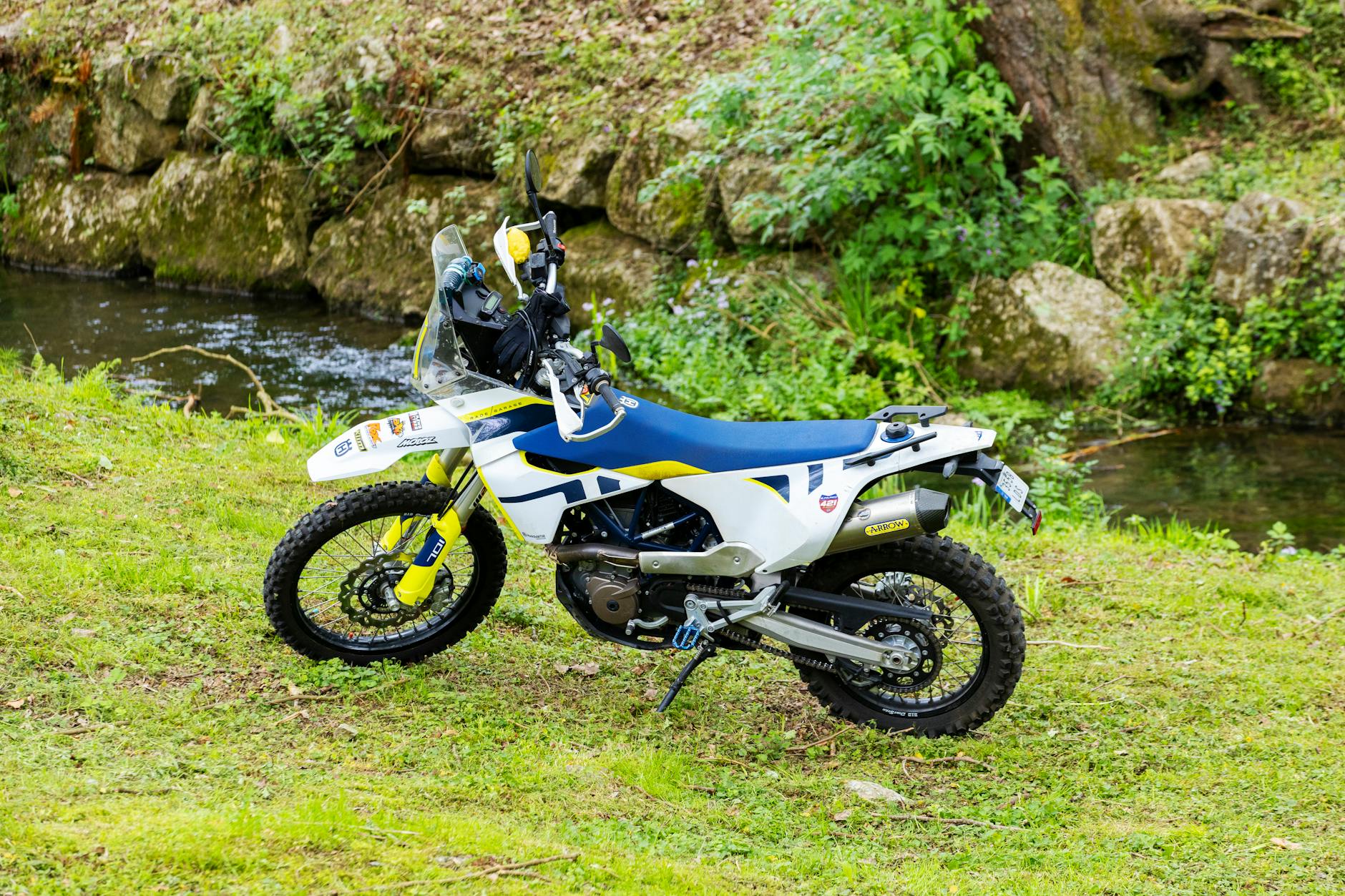 Motocykl terenowy zaparkowany na trawie przy spokojnym strumieniu