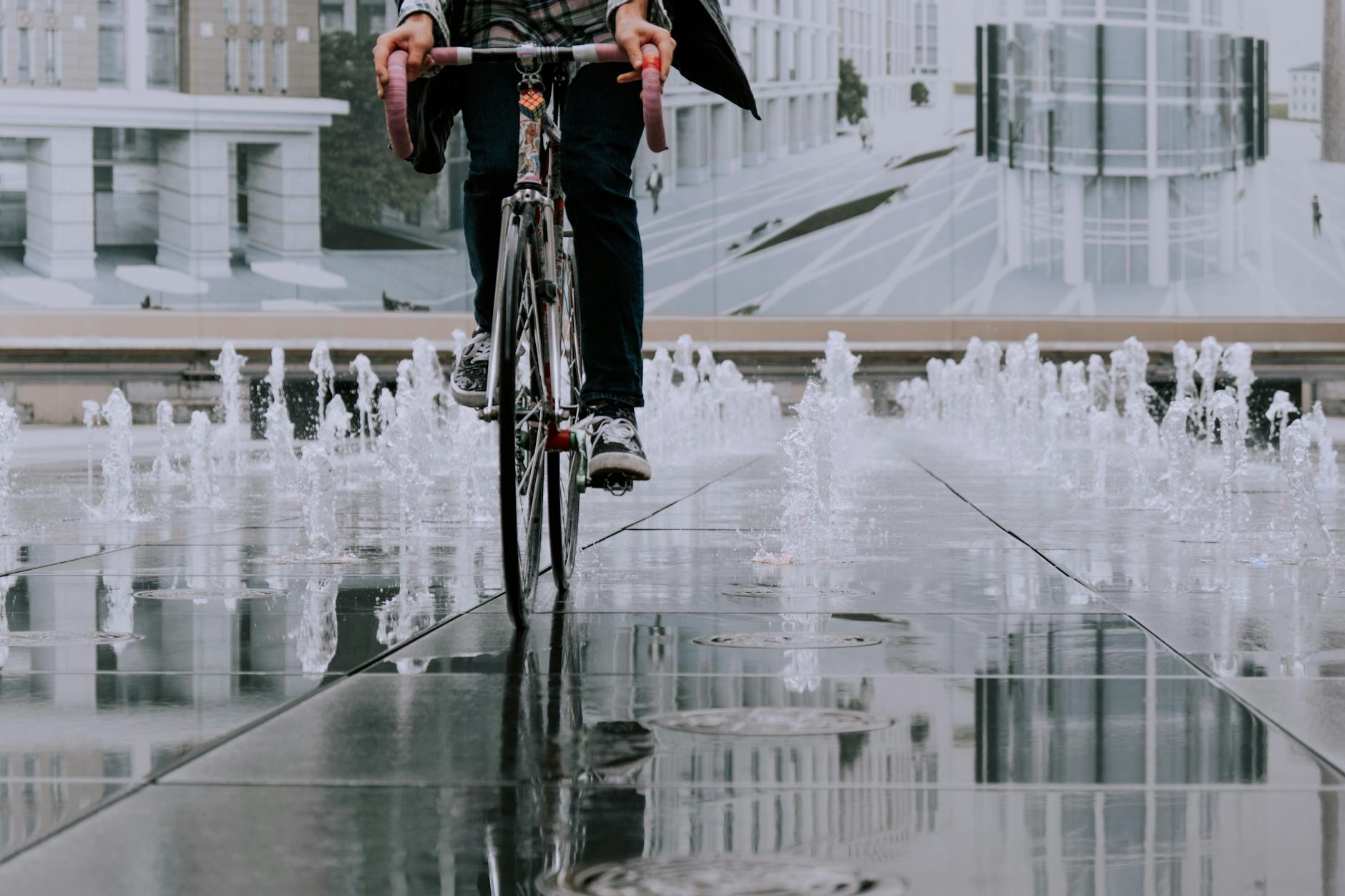 Rowerzysta przejeżdża przez miejską fontannę na tle nowoczesnych budynków