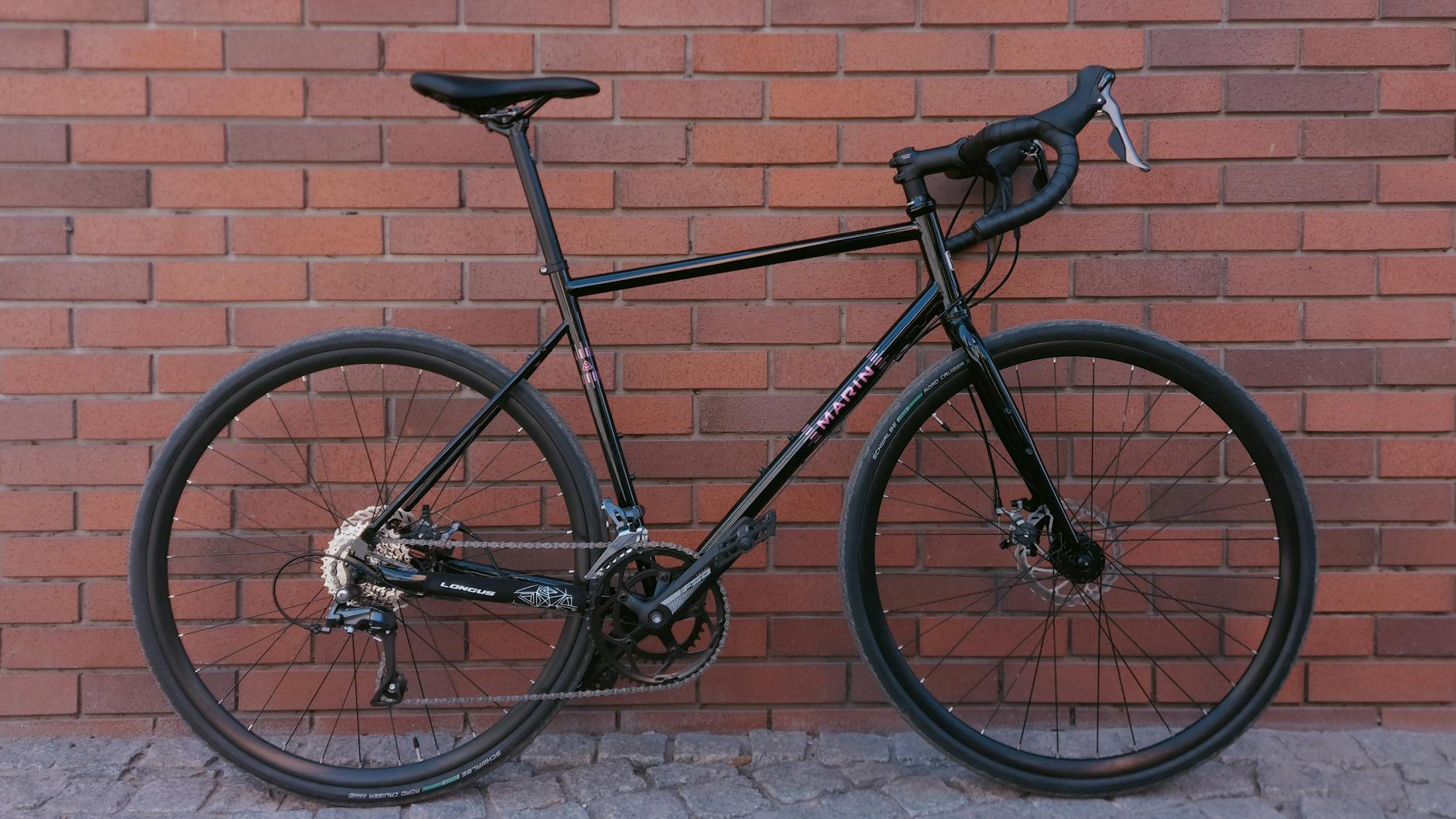 Czarny rower gravel oparty o czerwoną ceglaną ścianę