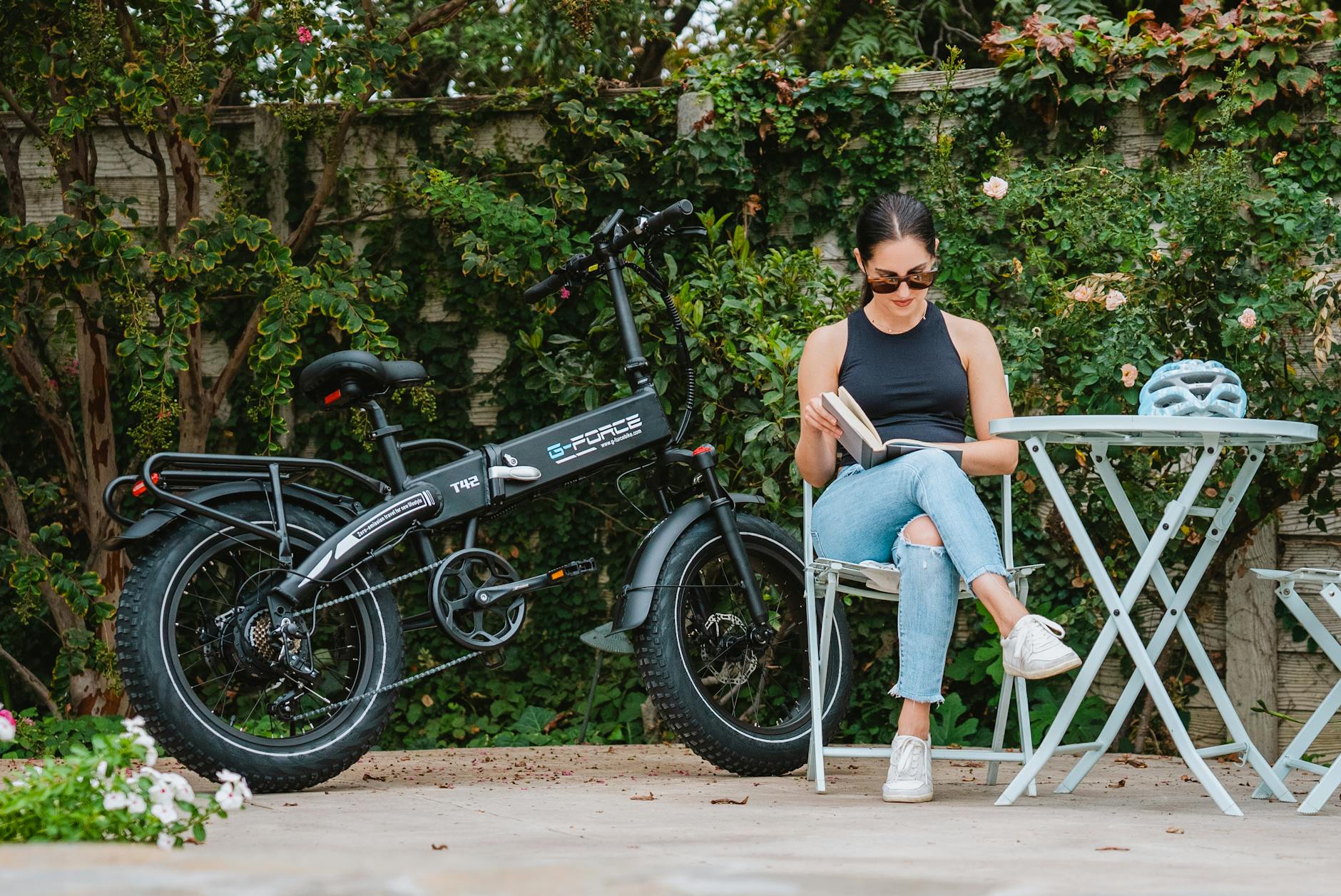 Kobieta czyta książkę obok elektrycznego roweru w ogrodzie