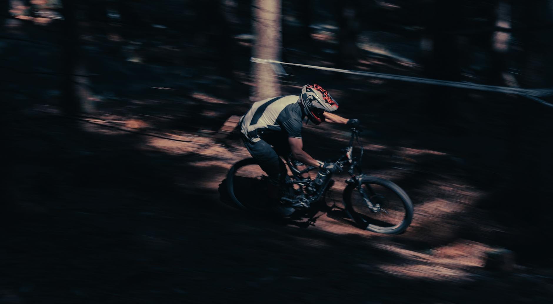 Kolarz MTB w kasku pędzi leśnym singletrackiem podczas zjazdu