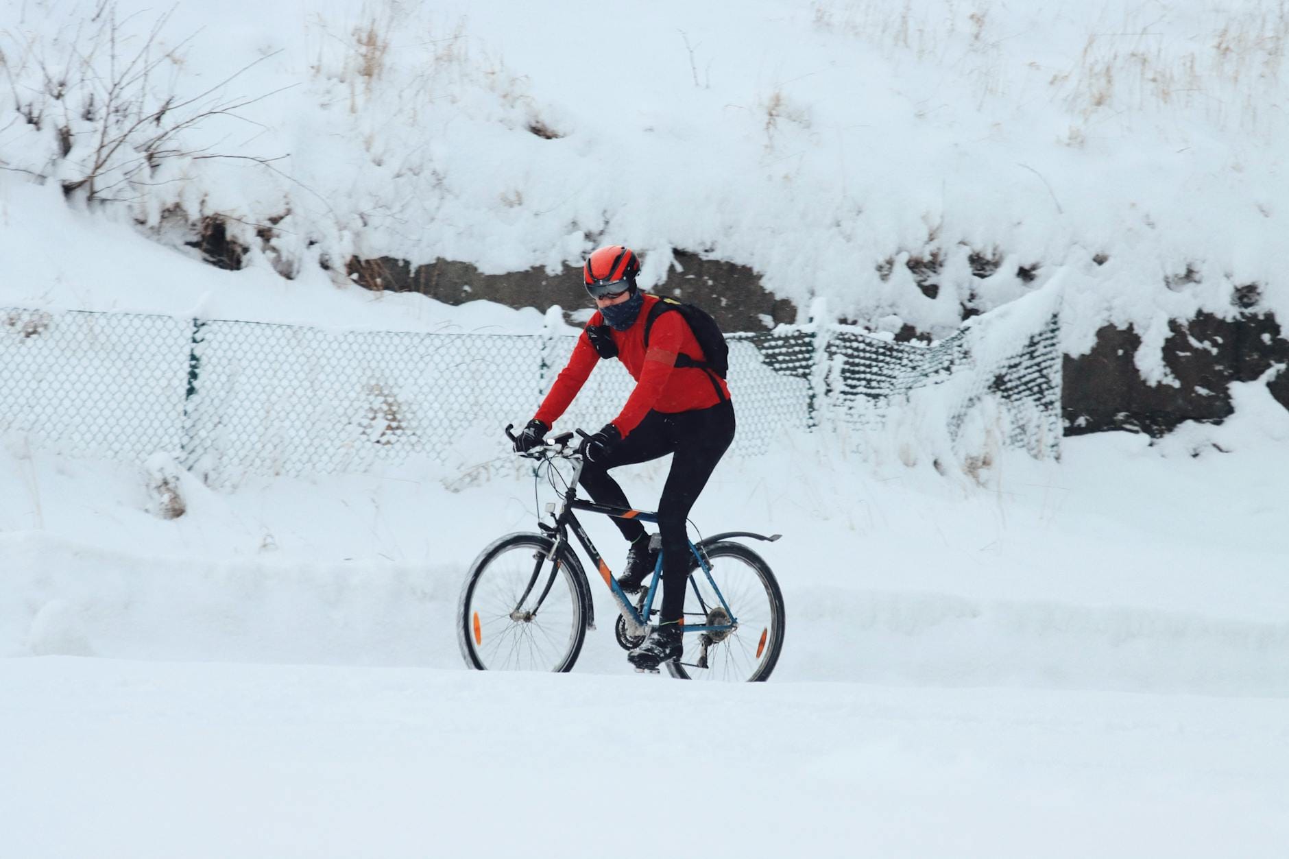 Rowerzysta w jaskrawym stroju jedzie zimą po ośnieżonej ulicy