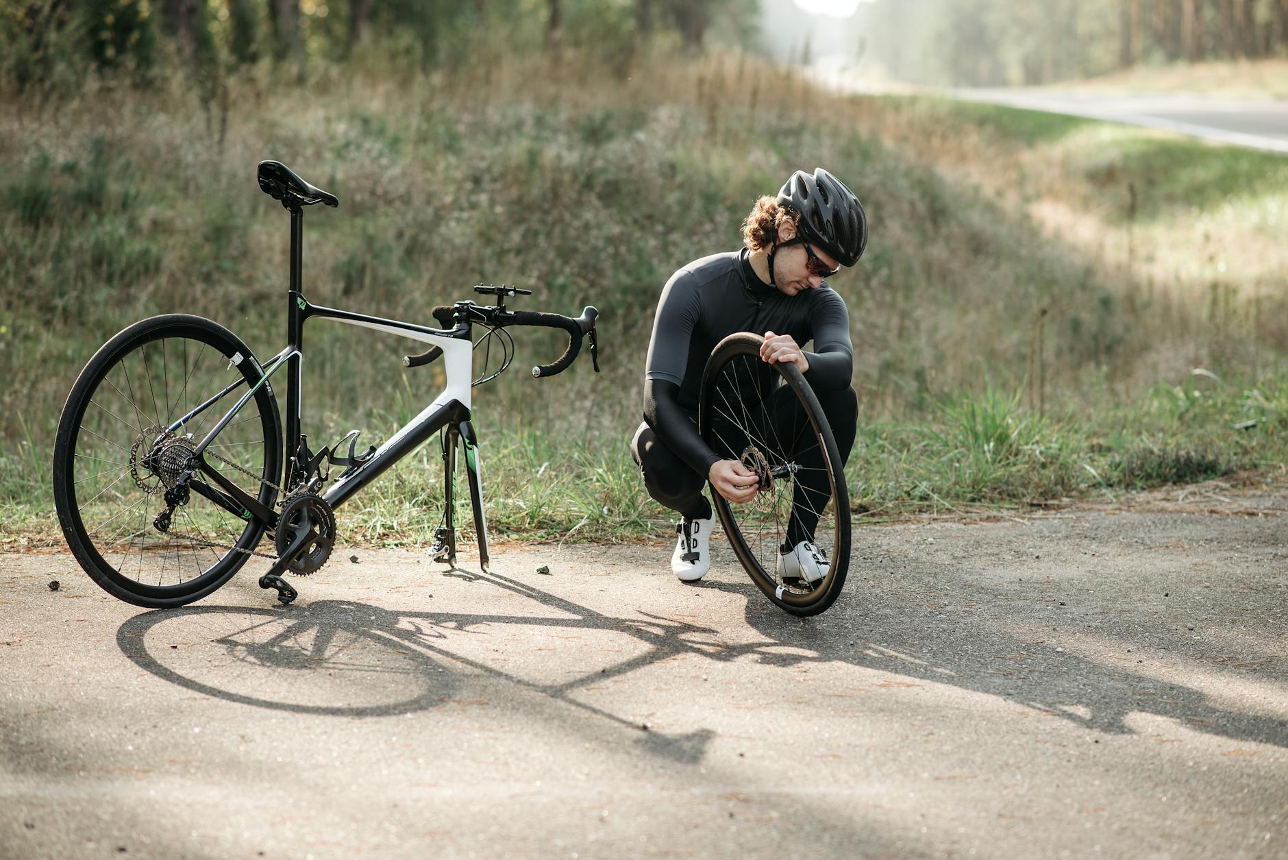 Rowerzysta w kasku naprawia przebitą oponę szosówki na wsi
