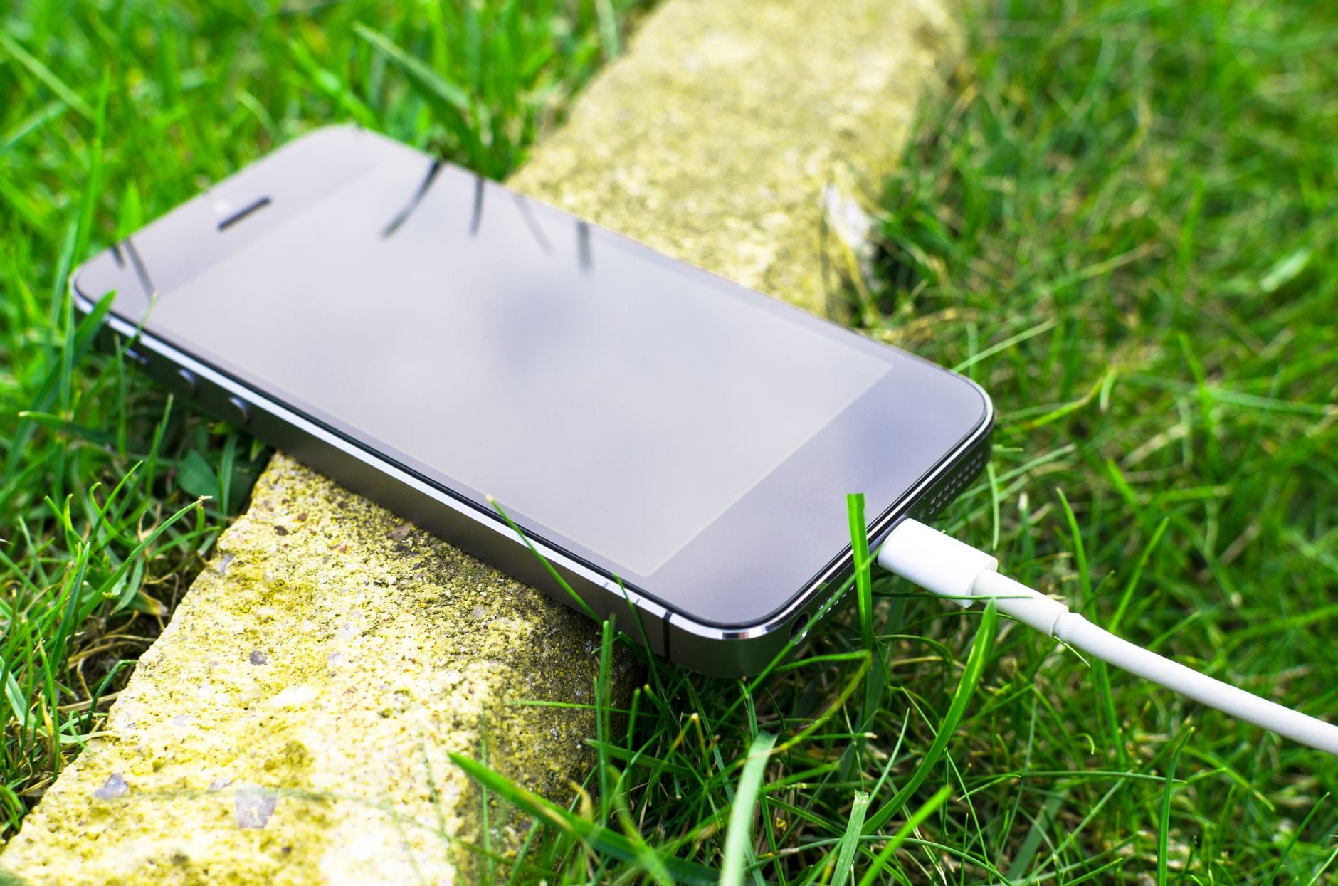 Smartfon ładowany kablem leży na trawie podczas postoju w trasie