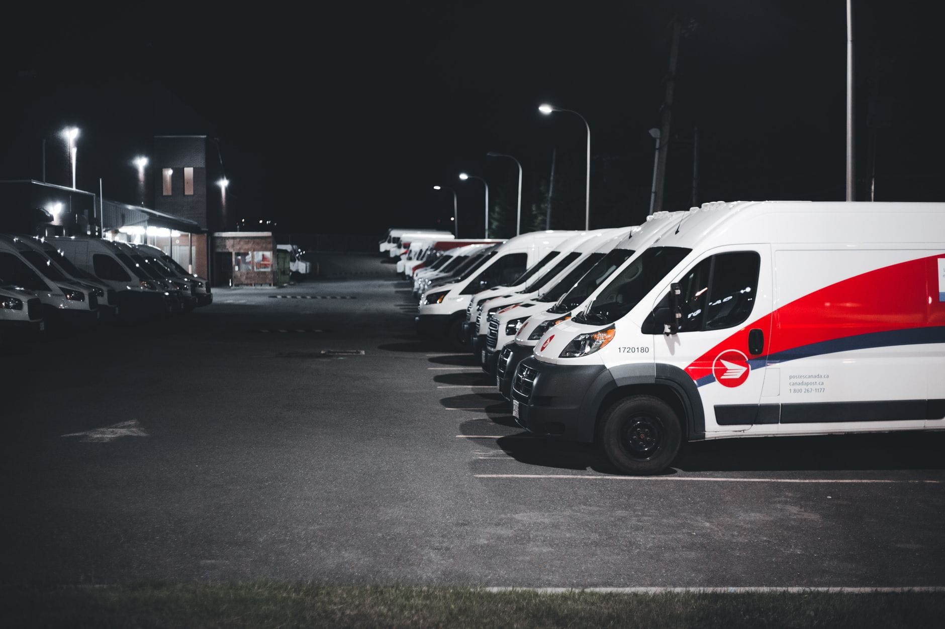 Białe i czerwone samochody dostawcze zaparkowane nocą na oświetlonym parkingu