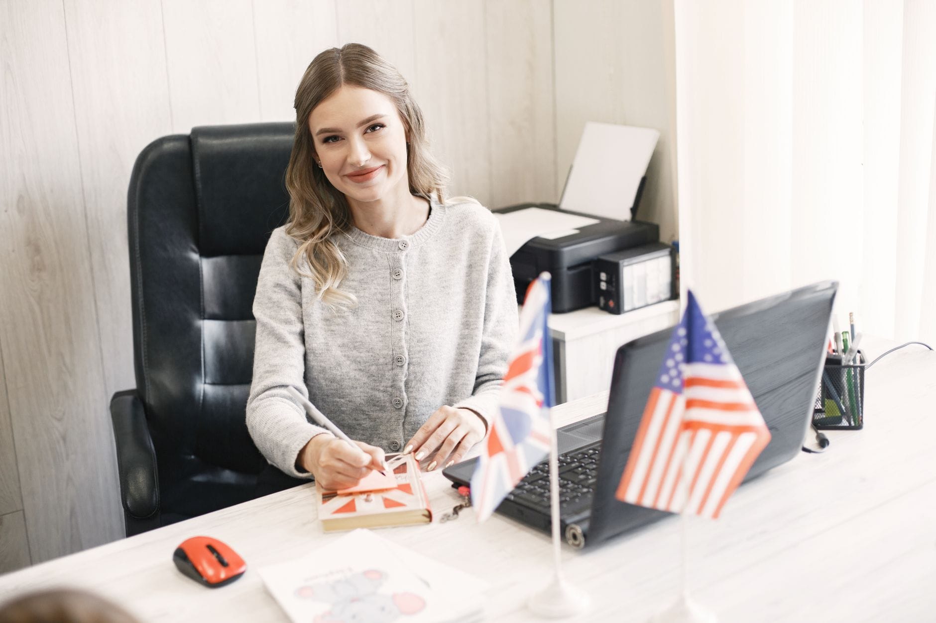 Uśmiechnięta bizneswoman przy biurku z flagami Wielkiej Brytanii i USA